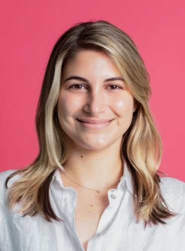 A woman smiling in front of a pink background.